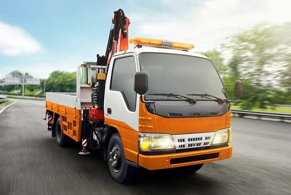 An orange and white tow truck is driving down a highway.