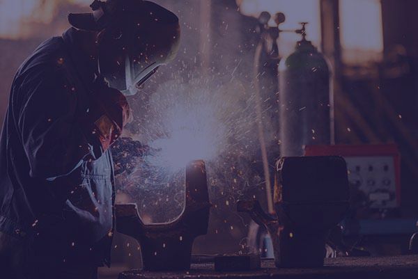 Welder wearing protective gear, working with bright sparks in a workshop.