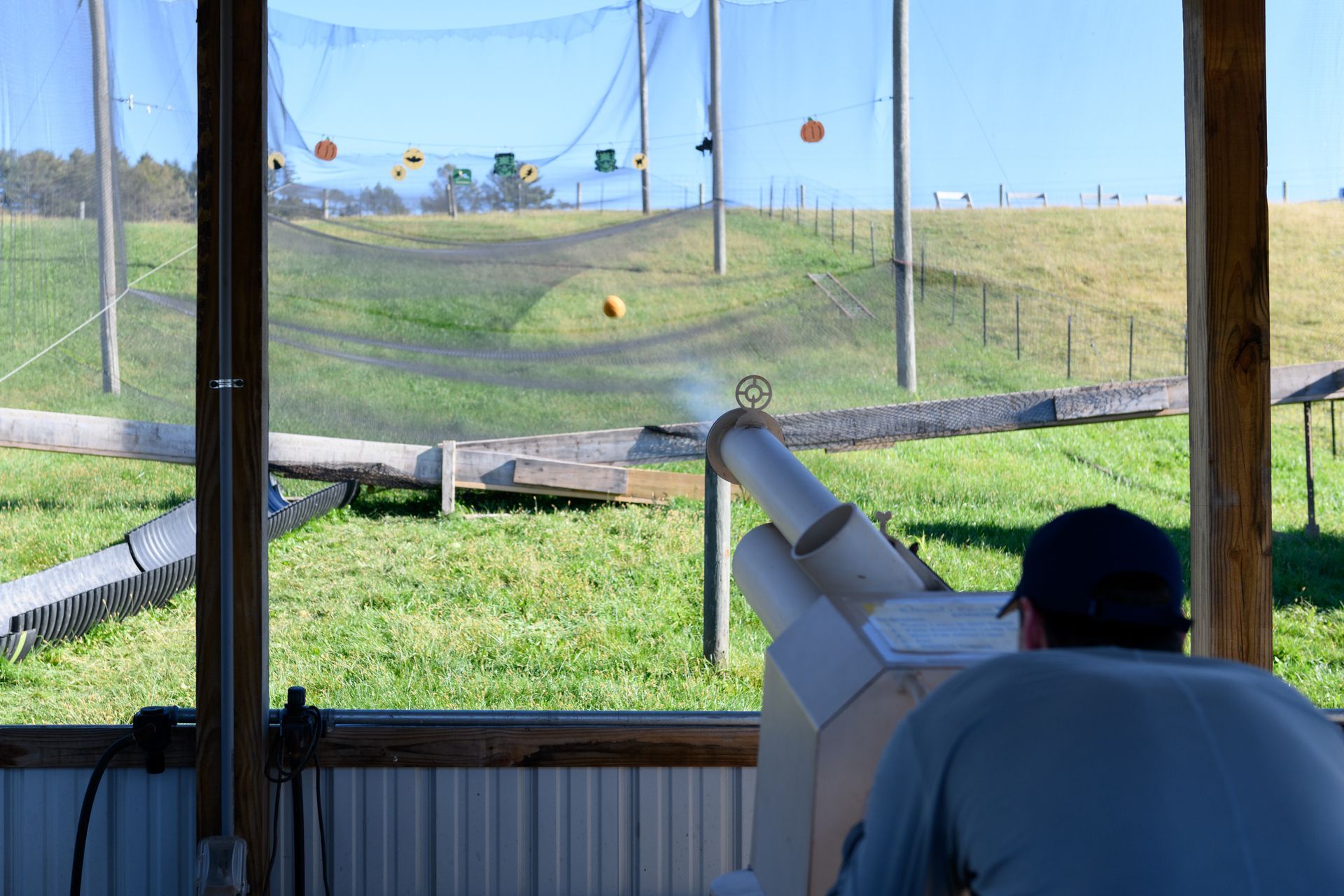 A person firing a cannon at targets on a green hill, enclosed by netting.