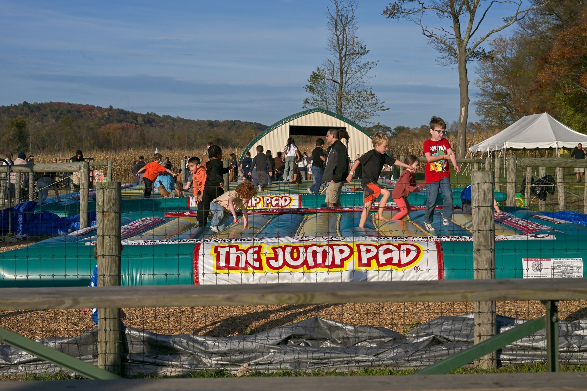 Two young boys playing on a colorful inflatable jumping structure outdoors. One boy is jumping.