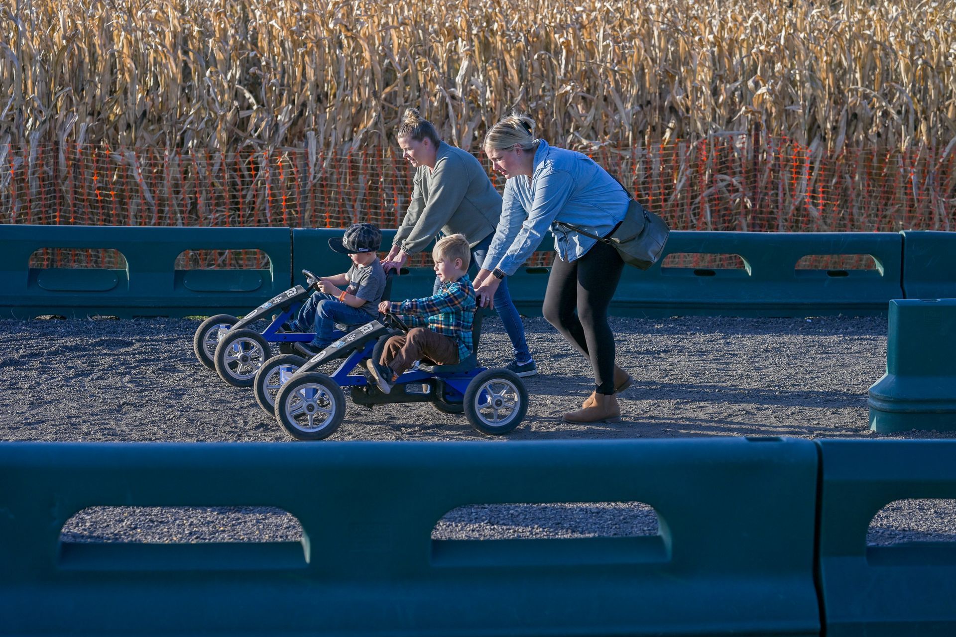 Boy smiles while driving a blue and black Blue Ridge Runner on a gravel track; green barriers line the path.