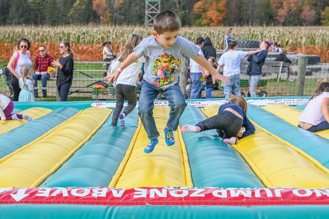 Boy jumping on a colorful inflatable playground with other children at an outdoor fall festival.