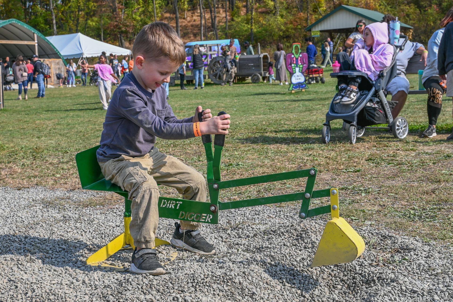 Boy playing on a green and yellow toy excavator at an outdoor event.