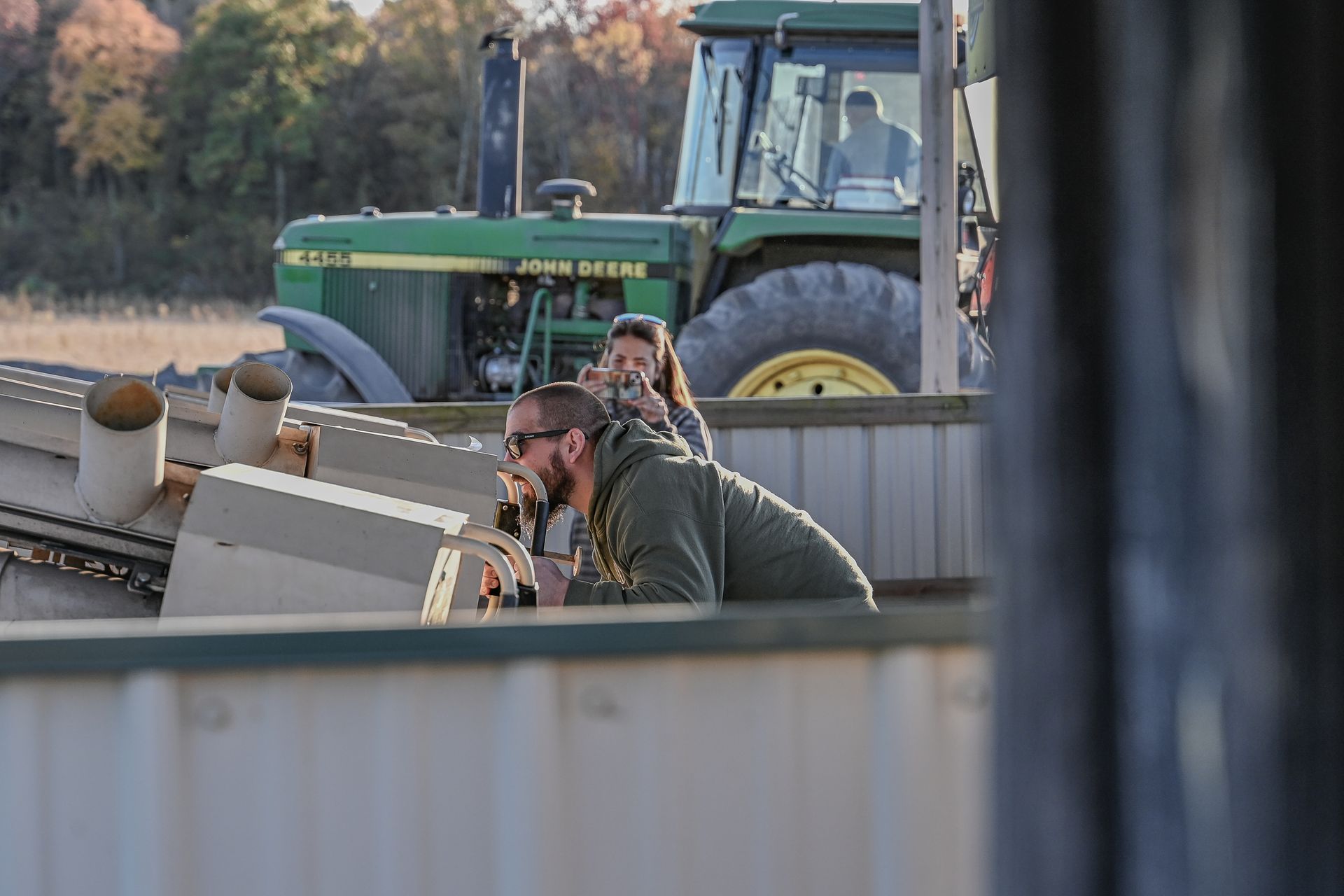 Man and woman near industrial equipment with a John Deere tractor in the background; outdoors.
