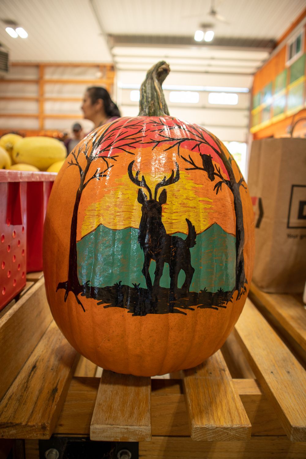 A pumpkin with a deer painted on it is sitting on a wooden shelf.
