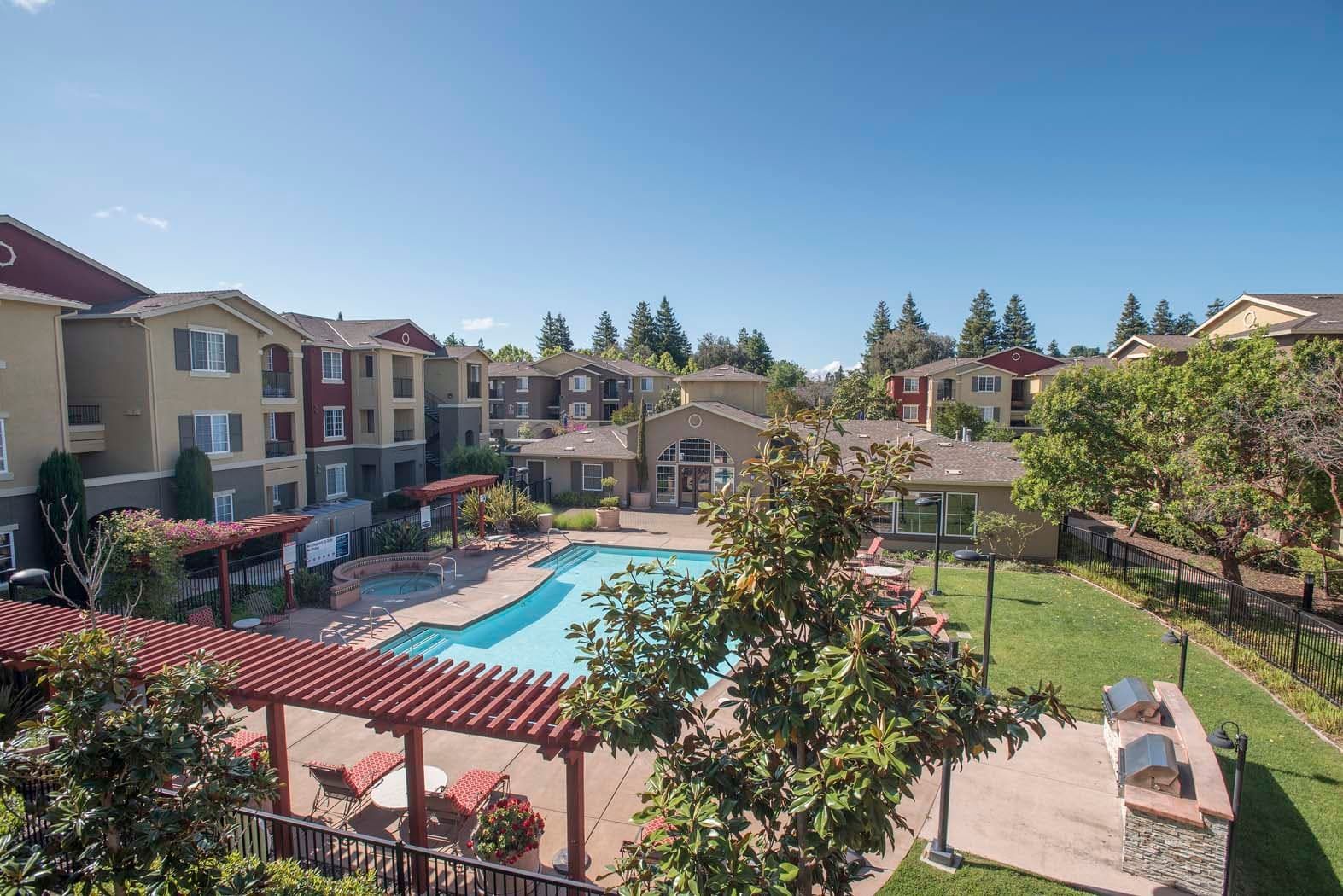Aerial view of an apartment complex featuring a swimming pool, lounge area, and surrounding greenery.