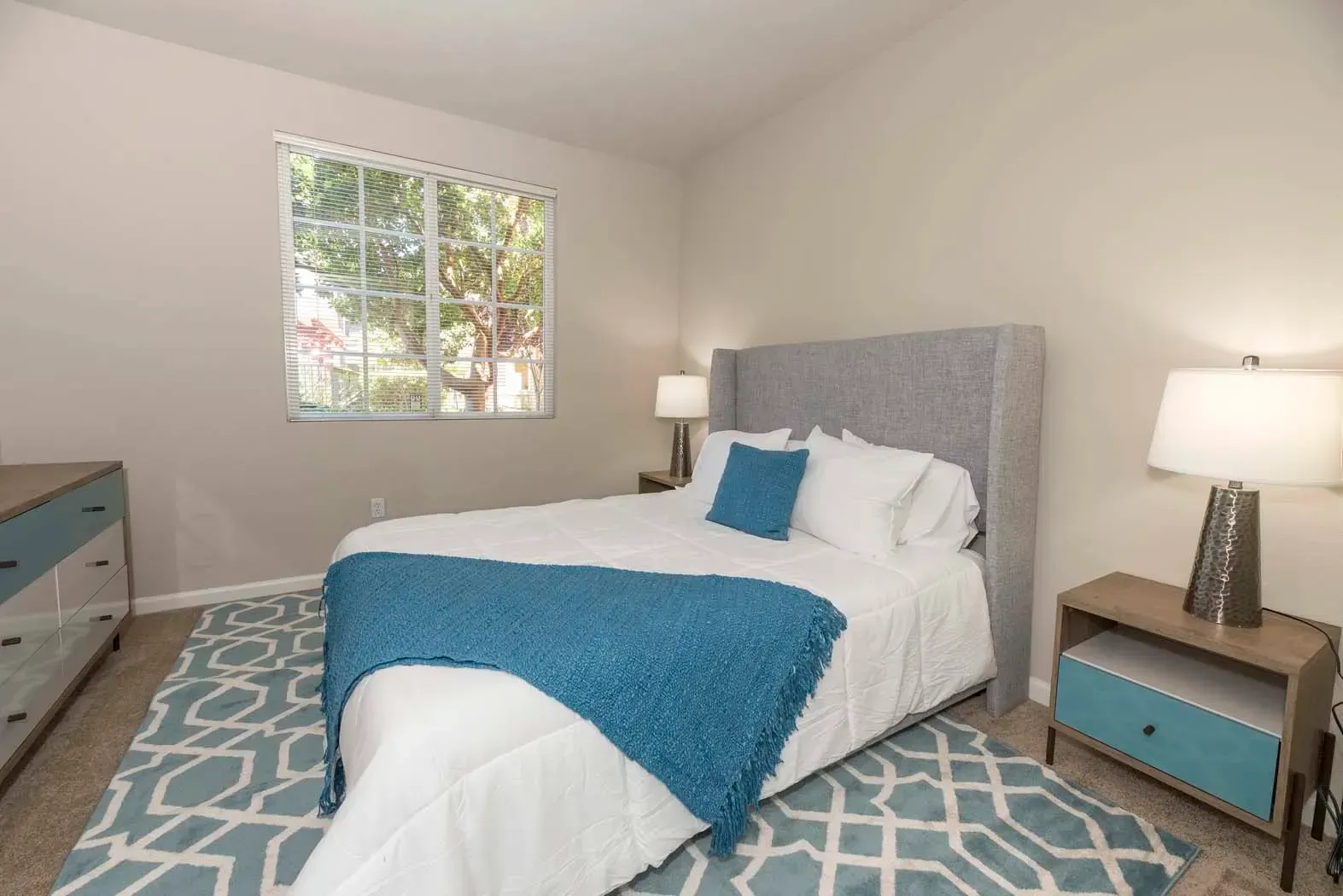 Cozy bedroom with a queen bed, decorative blue blanket, and wooden furniture