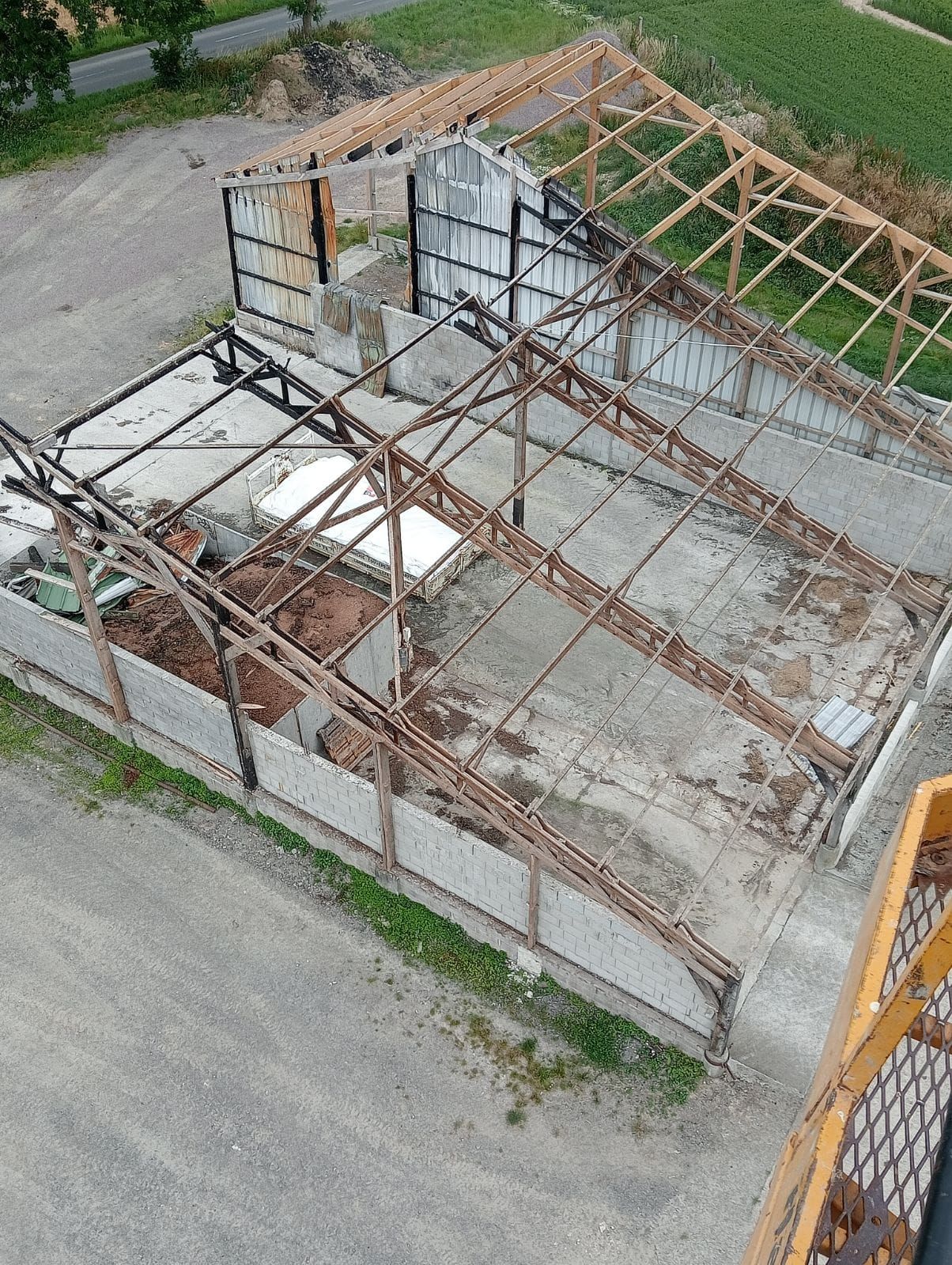Bâtiment agricole partiellement démoli, avec charpente en bois apparente et murs en béton.