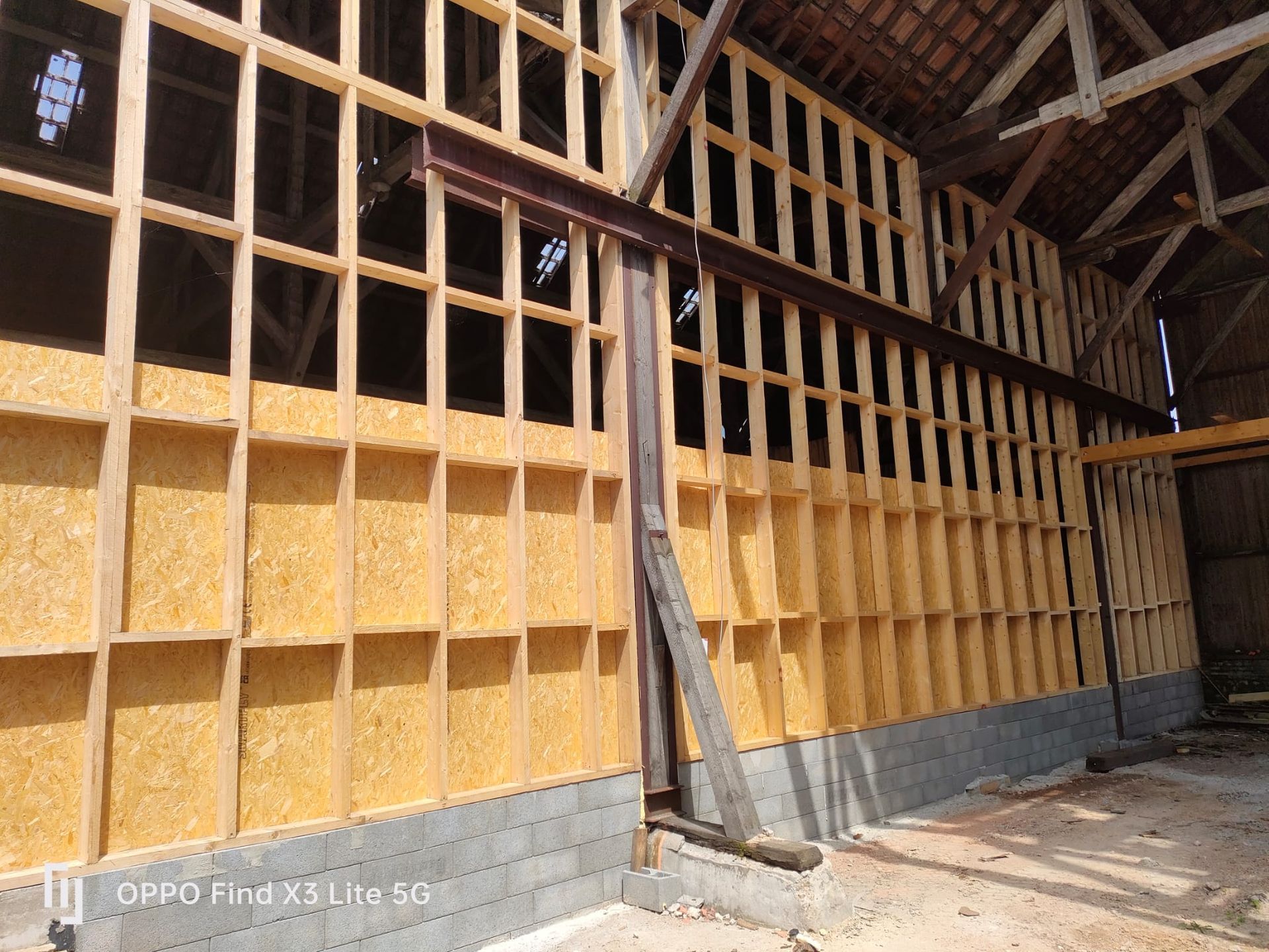 Intérieur d'un bâtiment en construction, montrant une ossature en bois isolée et une poutre métallique.