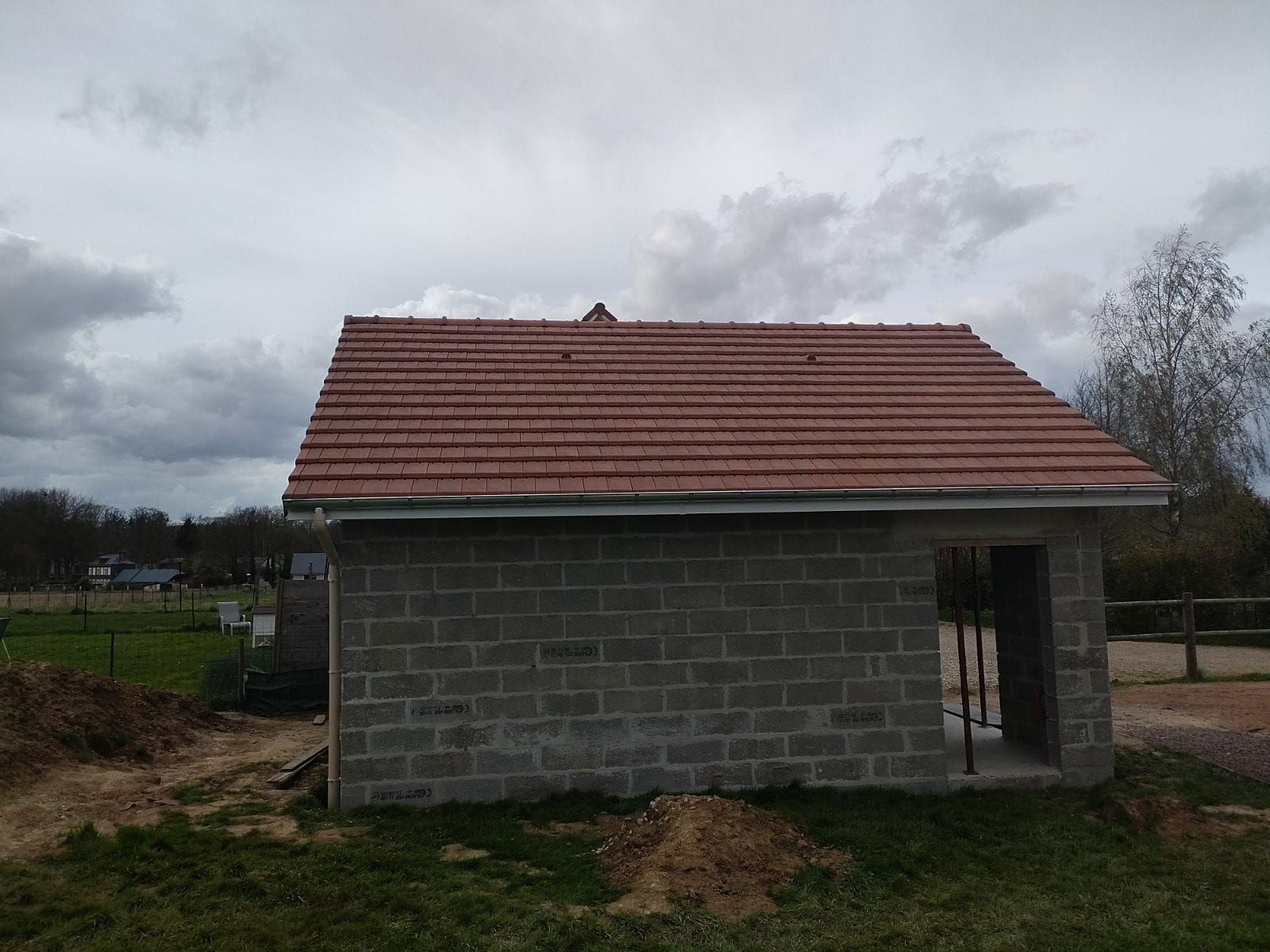 Construction d'un petit bâtiment en parpaings de béton avec un toit de tuiles rouges, situé à l'extérieur