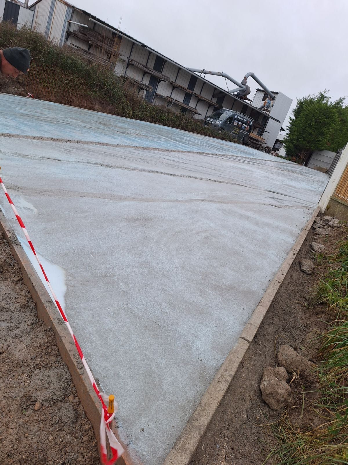 Surface en béton fraîchement coulée, en pente. Matériel de construction et de chantier en arrière-plan.