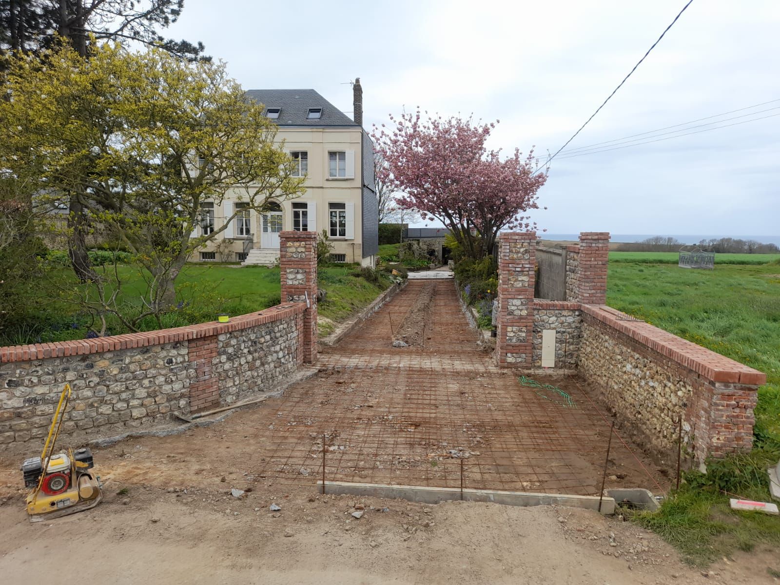 Allée en construction avec un mur de pierre et de brique menant à une maison en milieu rural.