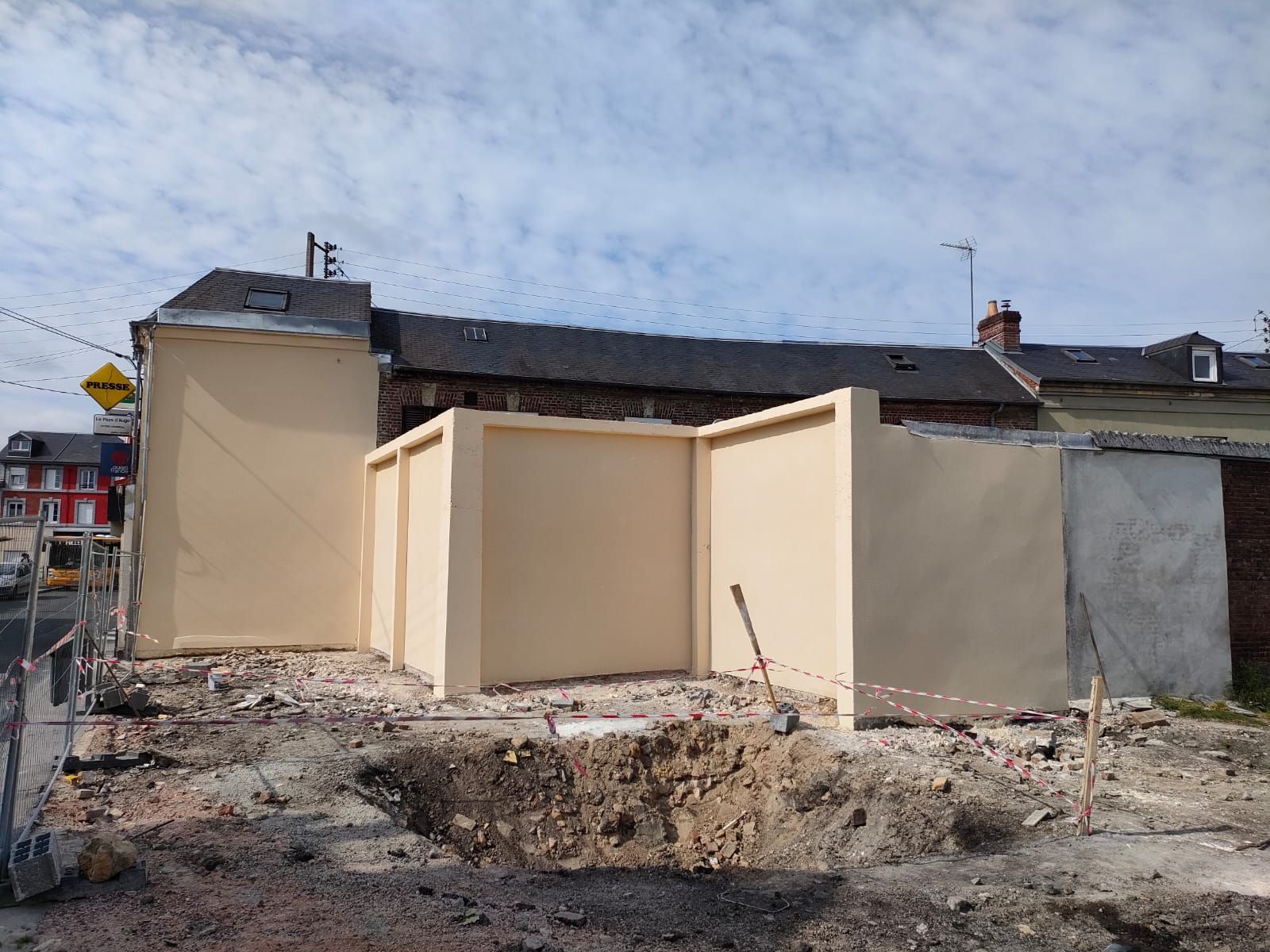 Chantier : des murs beiges sont en construction à côté d'un bâtiment en pierre et en brique.