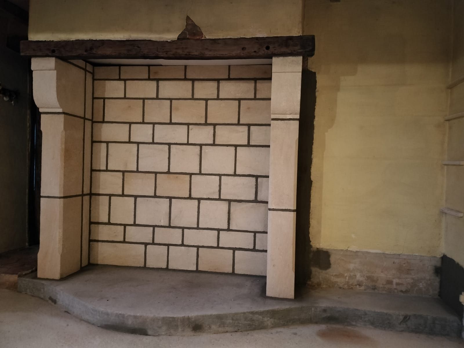 Cheminée en pierre avec intérieur en briques couleur crème, linteau en bois foncé et foyer arrondi en béton.