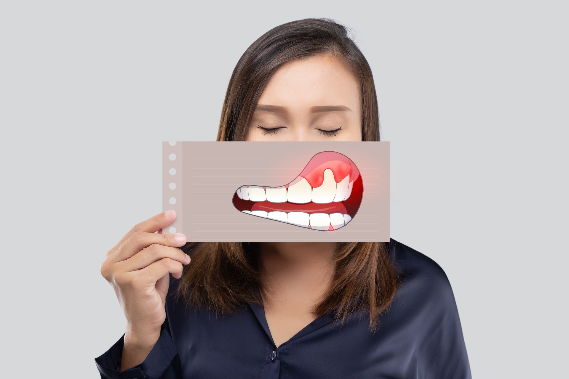 A person holds a card in front of their face depicting an illustration of swollen, inflamed gums and teeth.