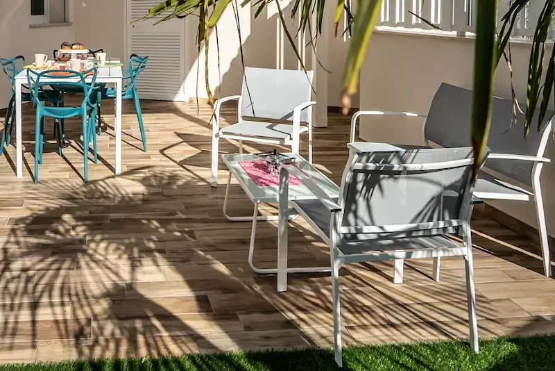 Sunny patio with turquoise and gray outdoor chairs around a glass table on a wooden deck
