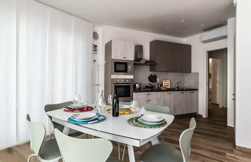 Bright modern kitchen-dining area with white chairs, table set, and gray cabinets
