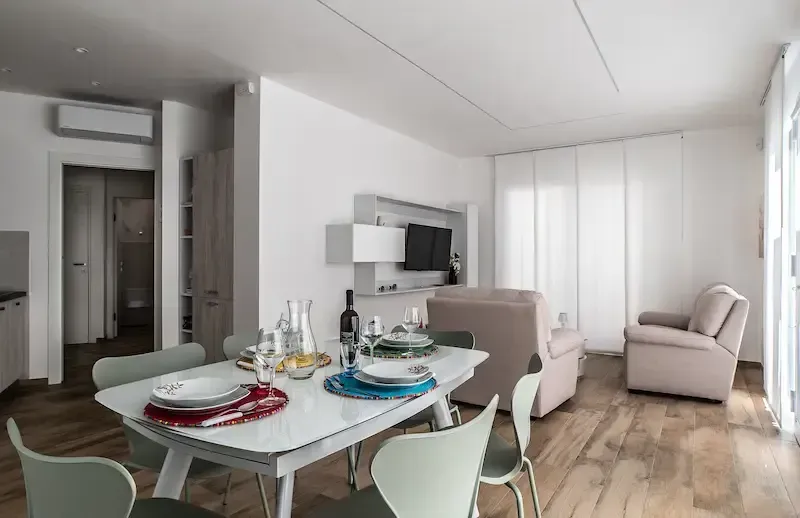 Modern open-plan dining room and living area with a set table, white walls, wood floor, and beige seating