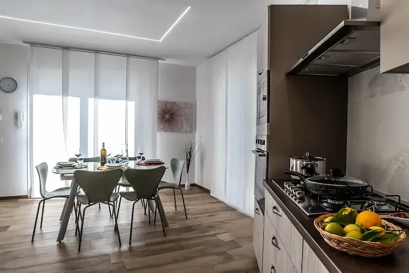 Modern kitchen and dining area with white cabinets, wood flooring, and a table set for four.