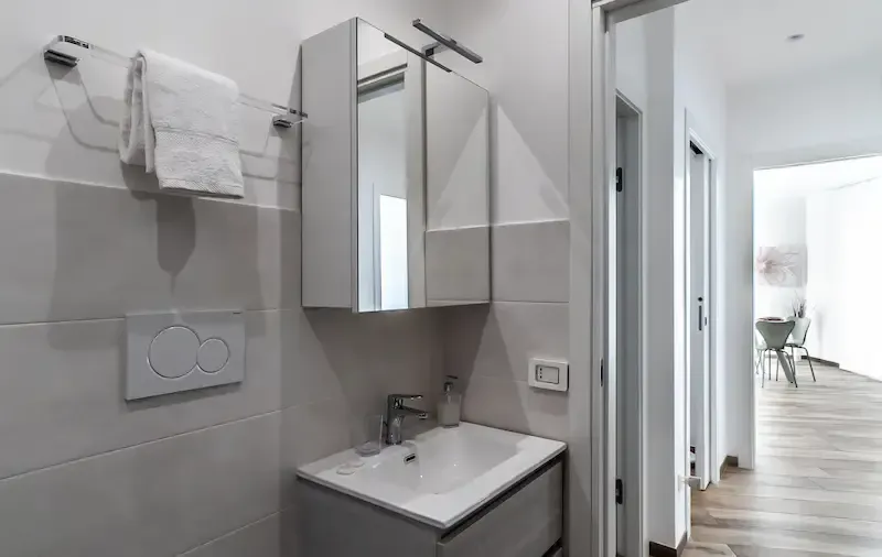 Modern bathroom with wall-mounted sink, mirror cabinet, and towel rack next to a doorway