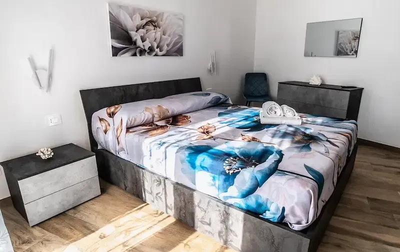 Bedroom with a black bed, blue floral bedding, two nightstands, and framed wall art.