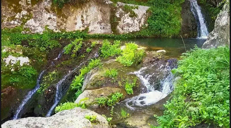 Small natural waterfall flowing over mossy rocks near an old Sicilian water mill.