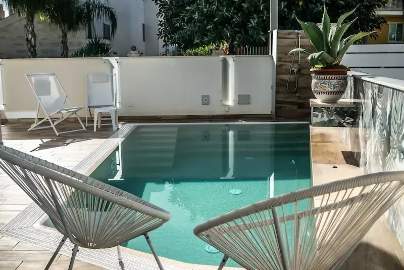 Modern outdoor pool area with woven lounge chairs and garden views at a Sicilian villa