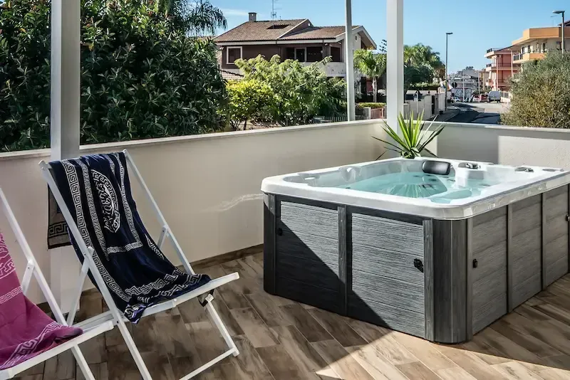 Terrace with a hot tub, lounge chairs, and a view of neighboring homes and greenery