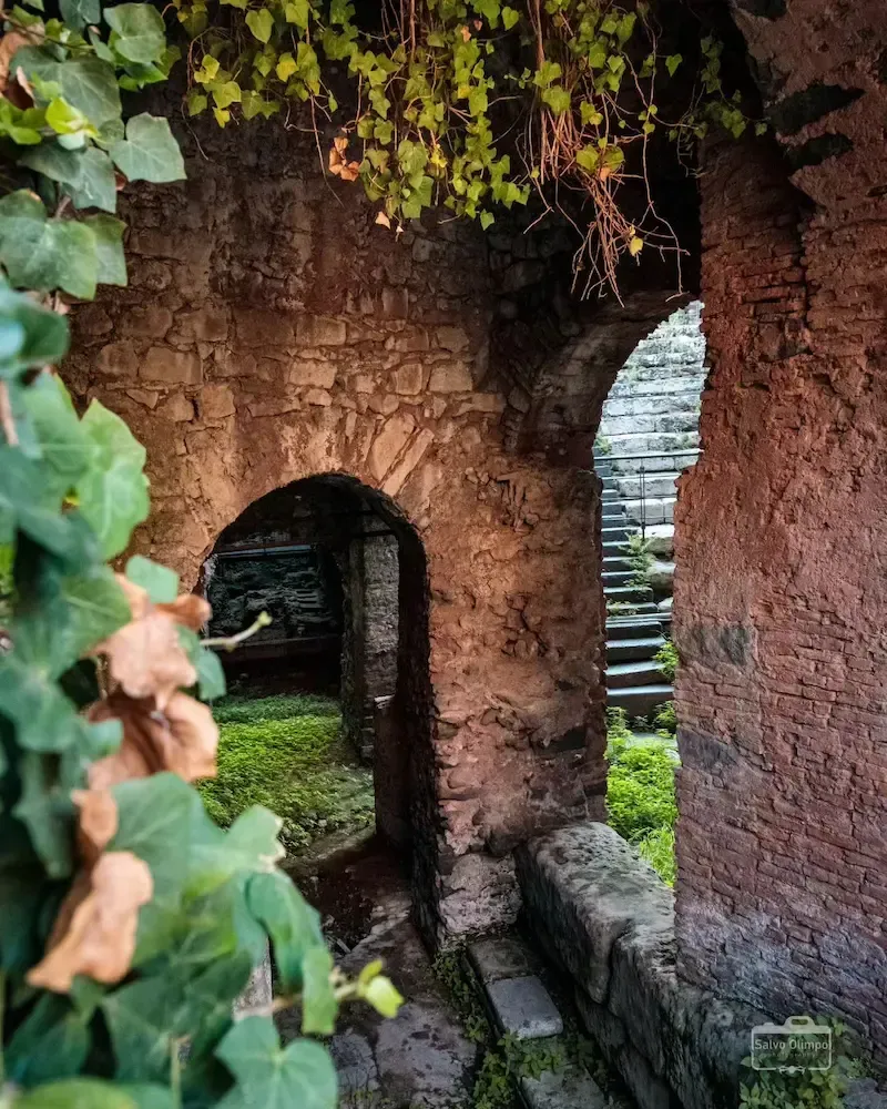 Ancient stone archway covered with greenery inside a historic Sicilian site