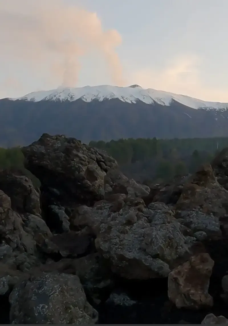 Mount Etna emitting smoke above black lava fields during volcanic activity