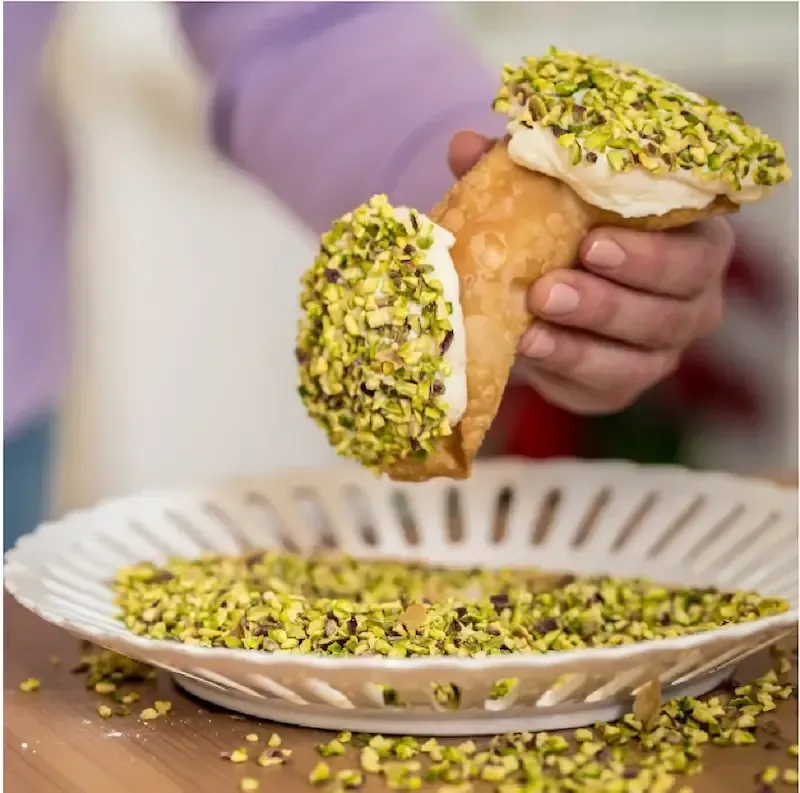 Hand holding a Sicilian cannoli covered with chopped pistachios