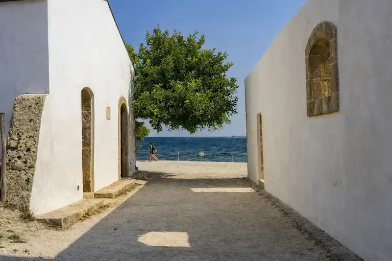 Narrow passage between whitewashed buildings in Vendicari with a tree at the end