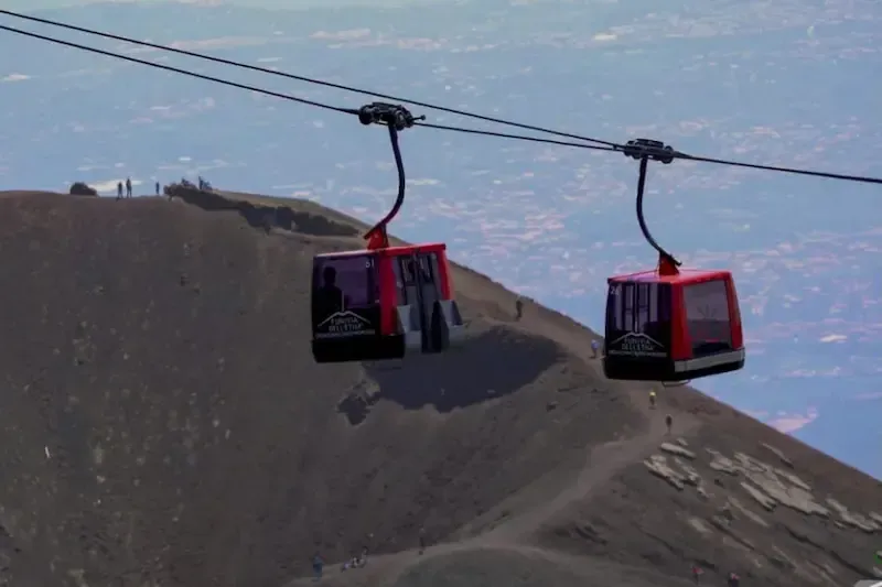Red cable cars ascending Mount Etna over volcanic slopes