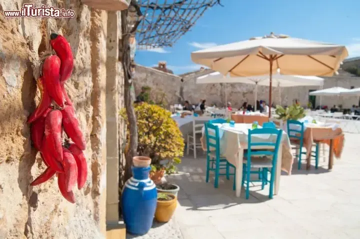 Traditional Sicilian courtyard in Marzamemi with stone walls, hanging peppers and blue chairs
