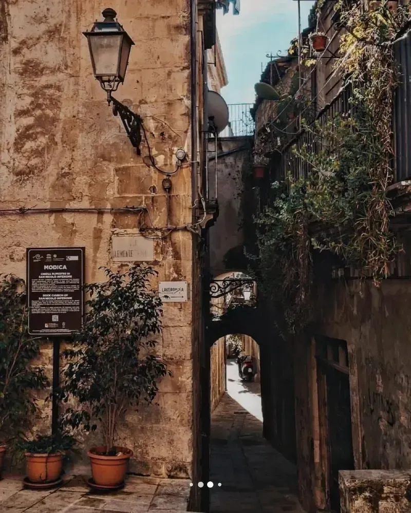Rustic alleyway in Modica with stone walls and an old street lamp