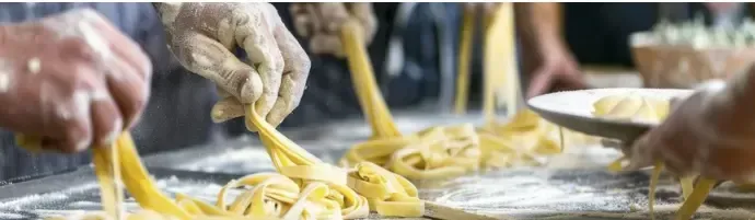 Hands shaping fresh Sicilian pasta on a wooden board.
