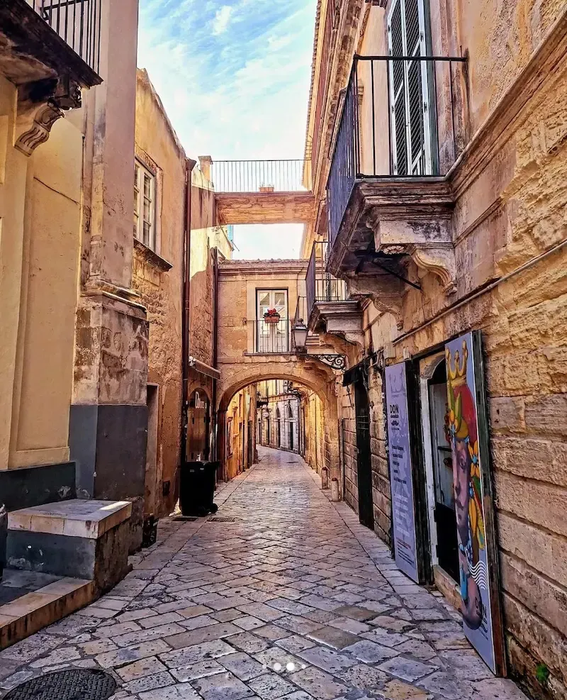 Narrow alleyway in Modica with historic stone buildings and balconies