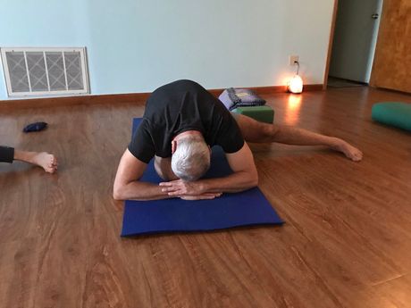 A man is laying on a yoga mat on a wooden floor.