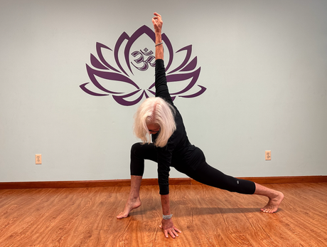 A woman is doing a yoga pose in front of a purple lotus flower on a wall.