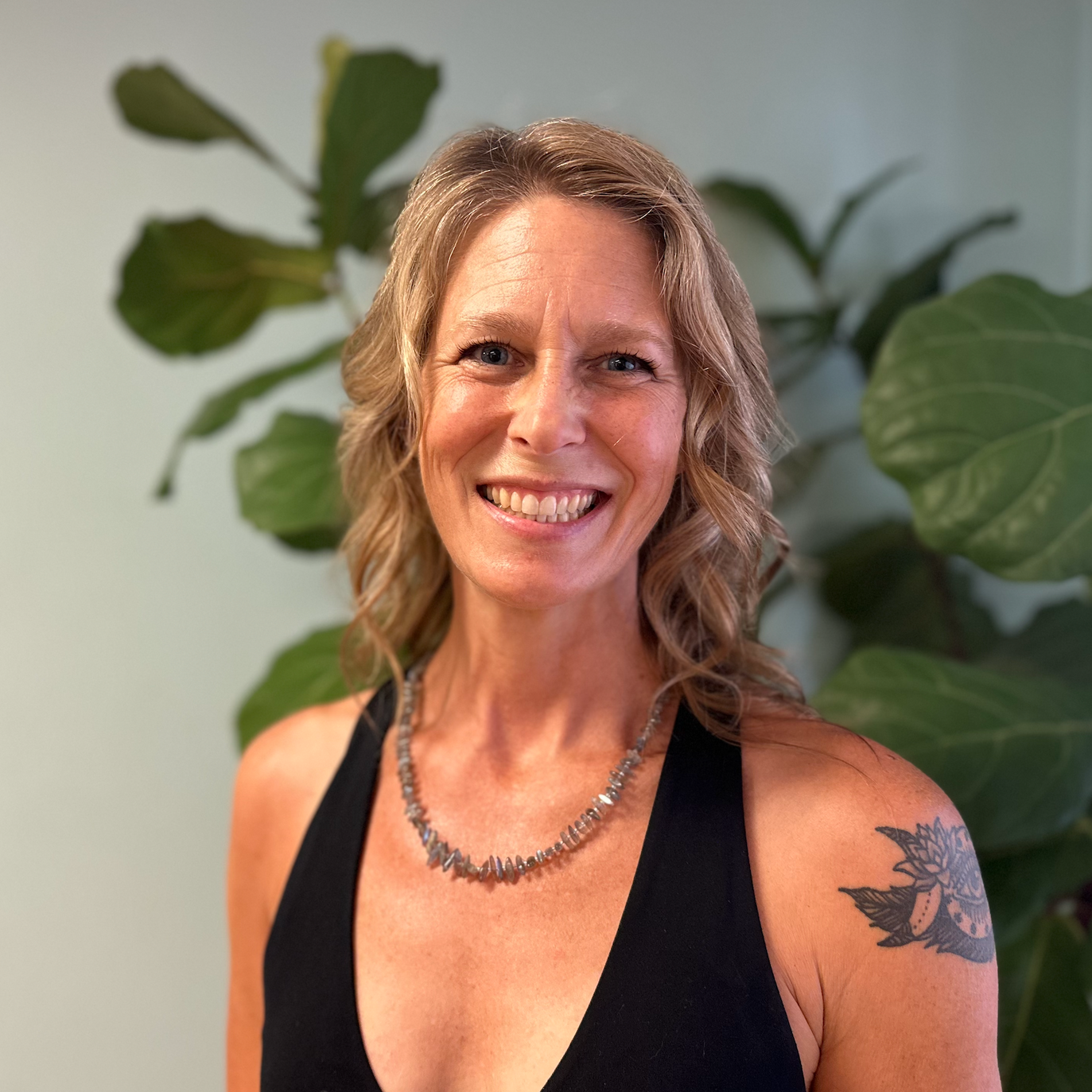 A woman with a tattoo on her arm is smiling in front of a plant