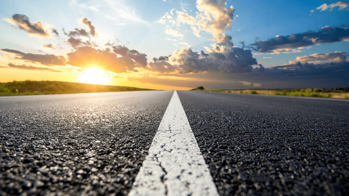 Low-angle view of a newly paved asphalt road with a bright center line stretching toward the horizon at sunset during an asphalt paving service in Centennial, CO