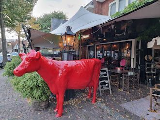 Voor een restaurant staat een standbeeld van een rode koe.