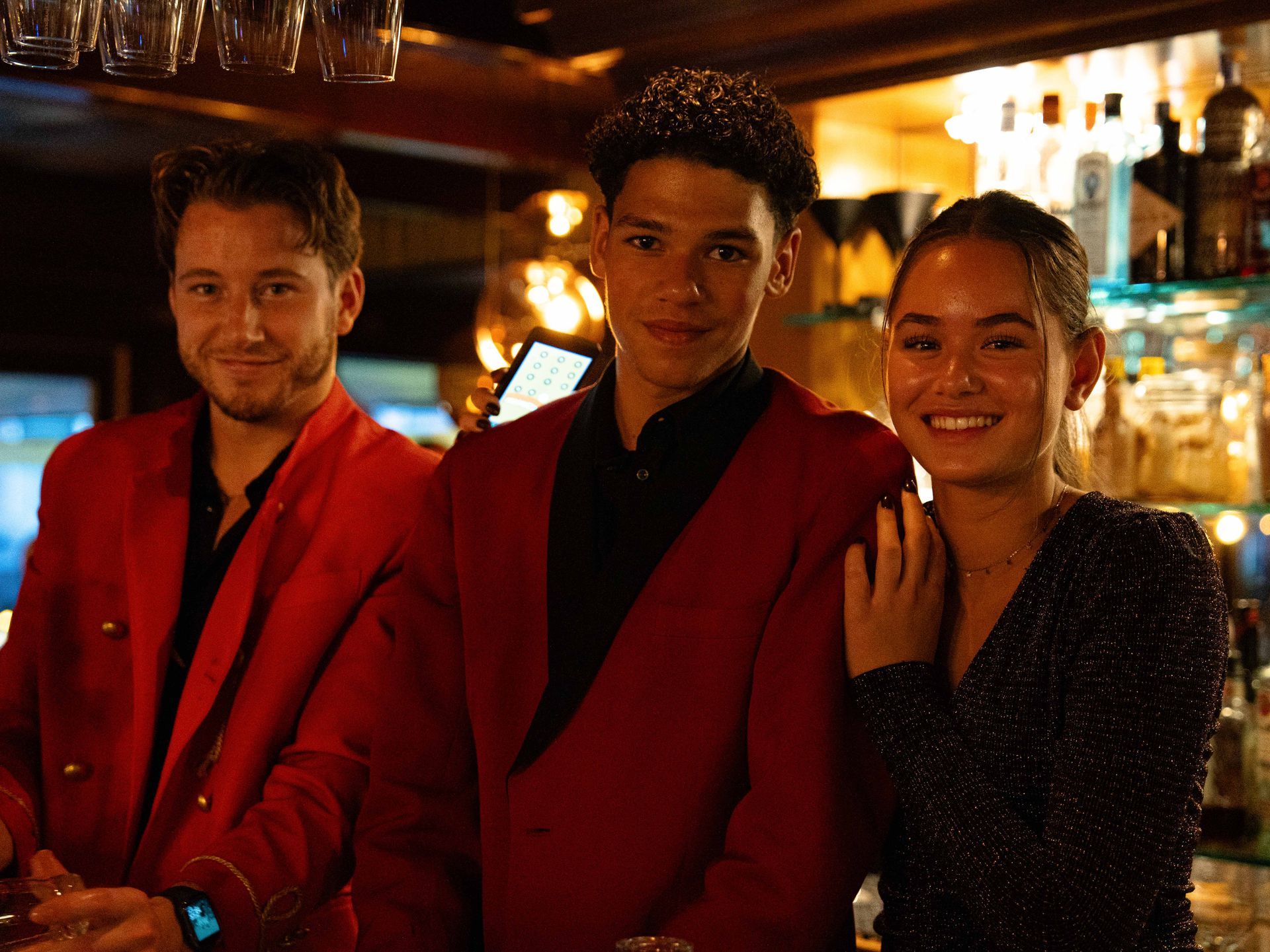 Drie mensen in rode jassen poseren voor een foto in een bar.