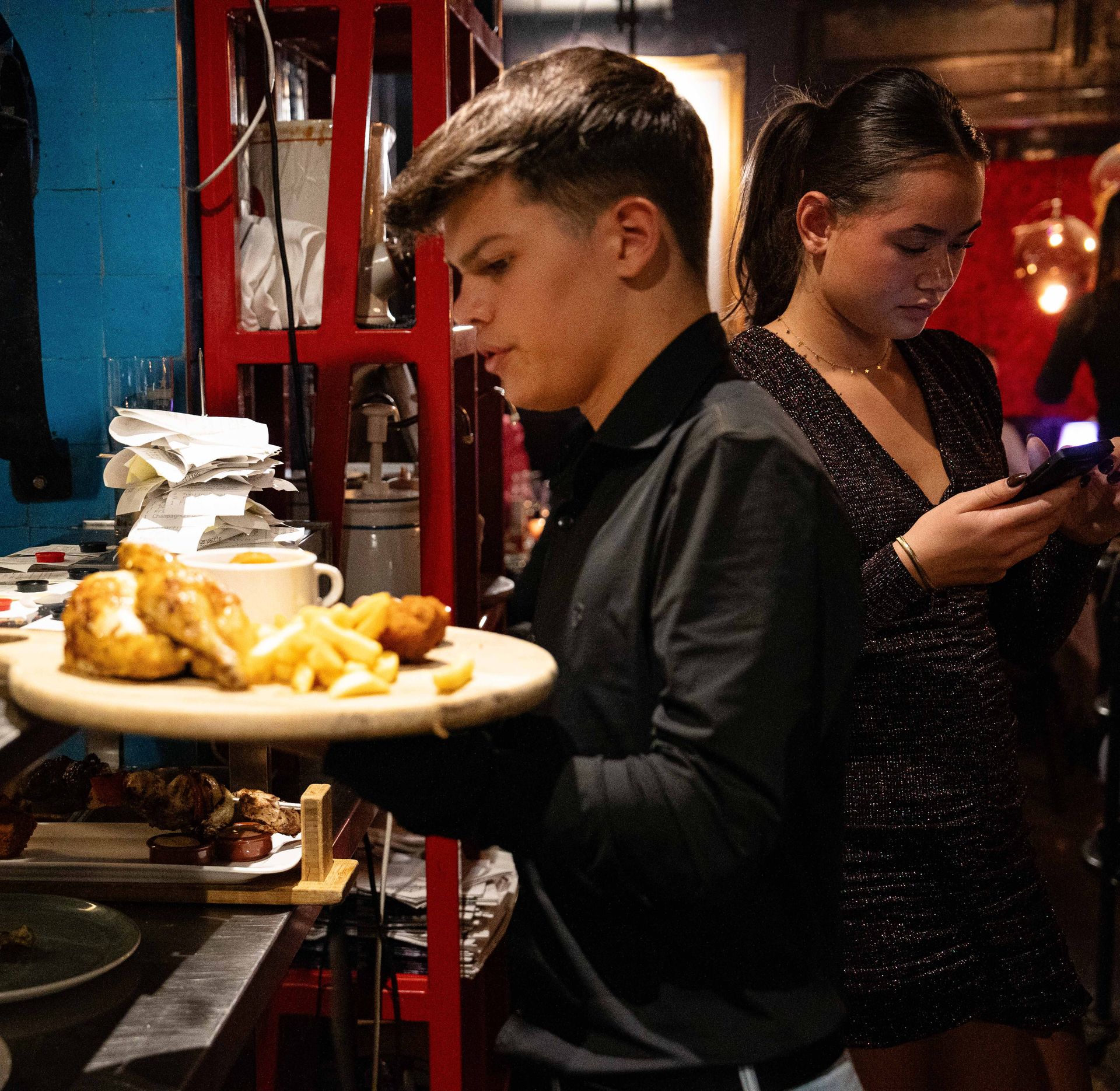 Een man houdt een bord met eten vast terwijl een vrouw naar haar telefoon kijkt.  Bij Linke Loetje