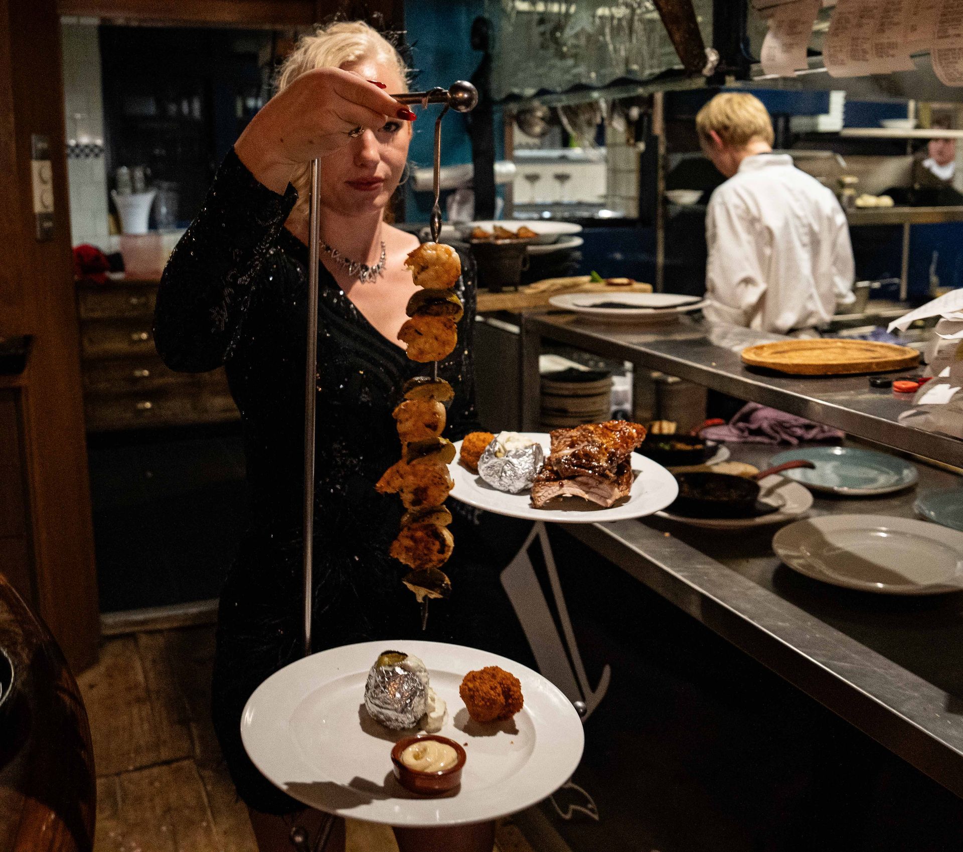 Een vrouw houdt een spies met voedsel vast in een keuken. Bij Linke Loetje