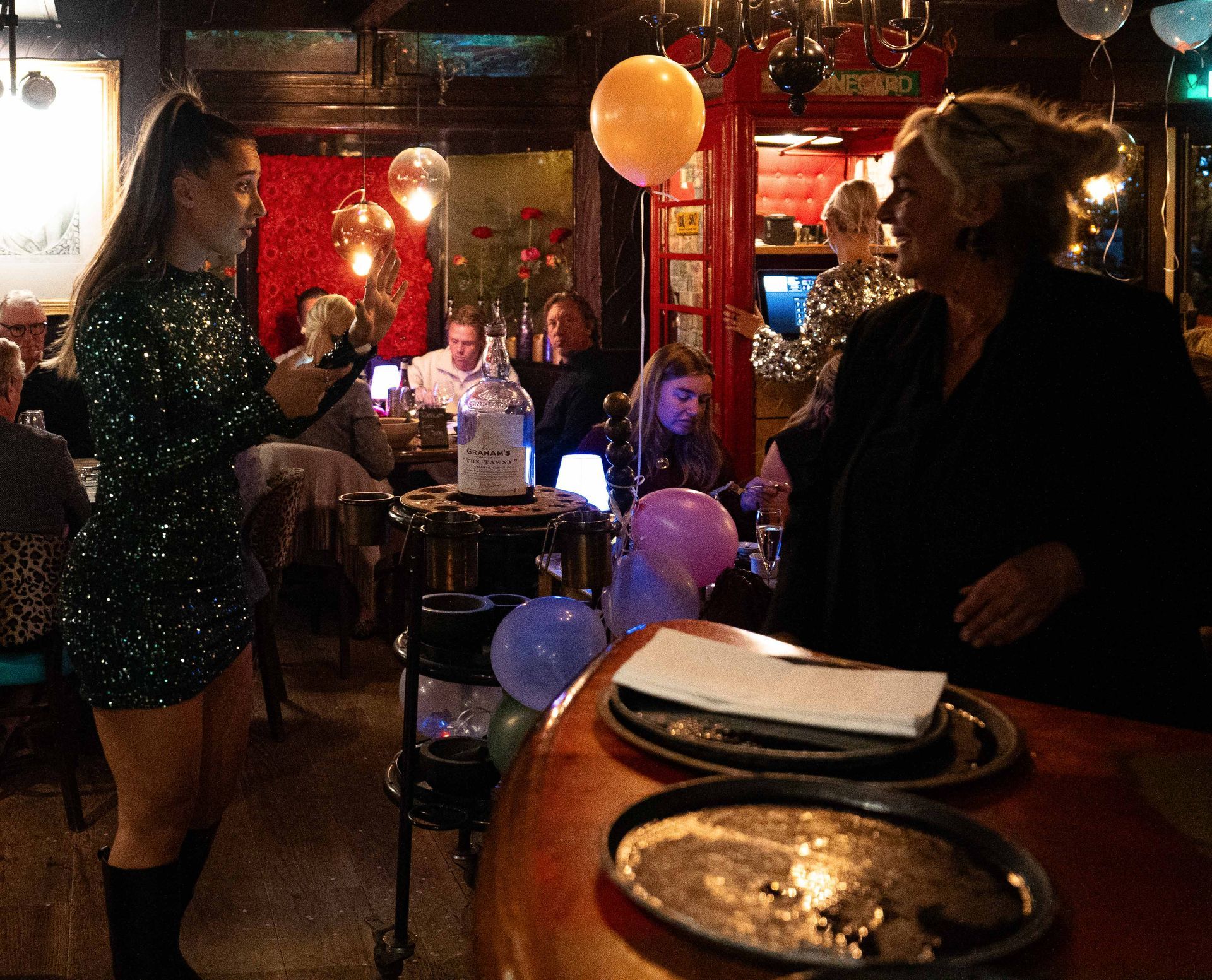 Een vrouw in een met pailletten bezette jurk zingt in een microfoon in een restaurant