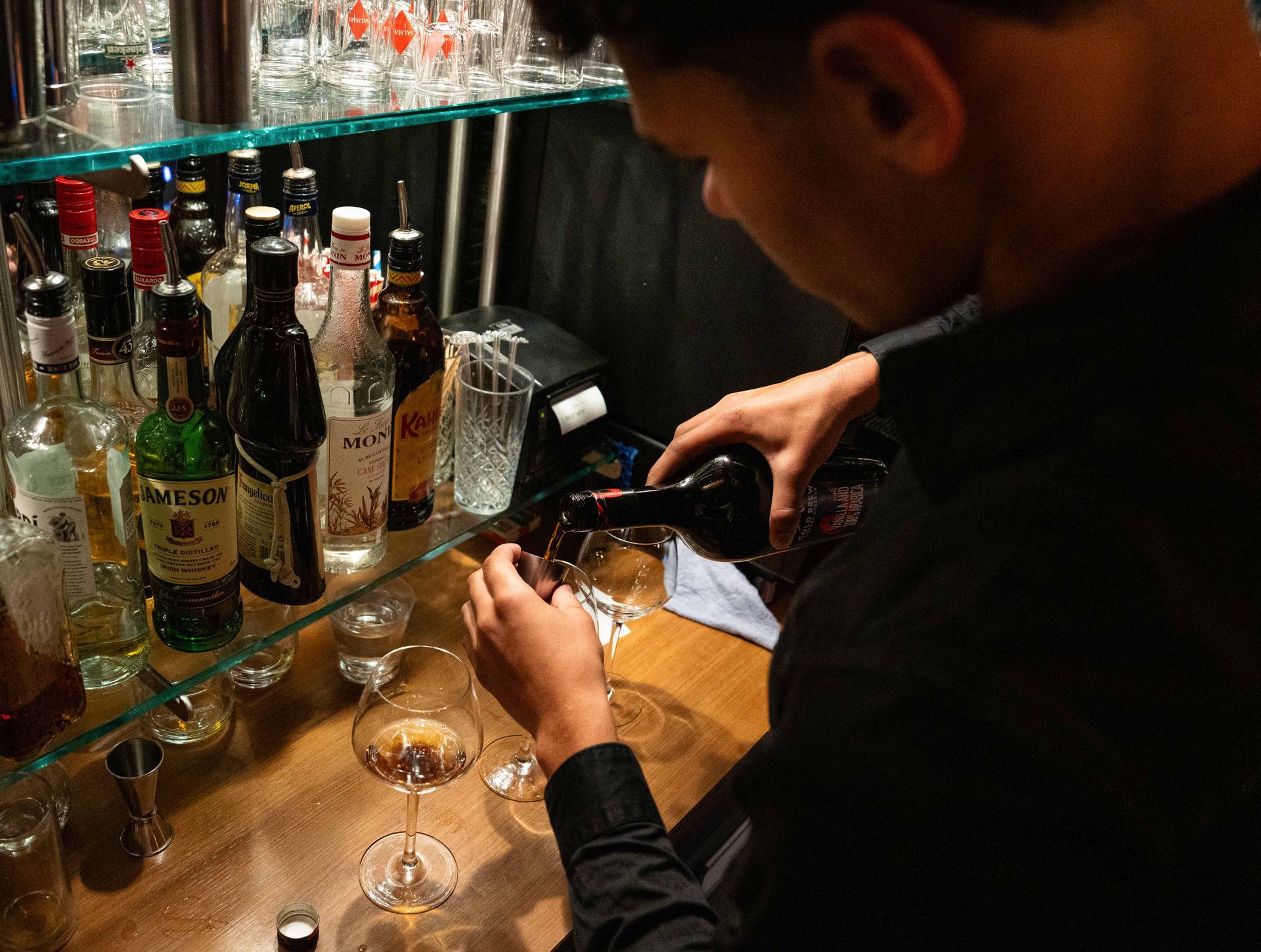 Een man giet een fles alcohol in een glas. Bij Linke Loetje