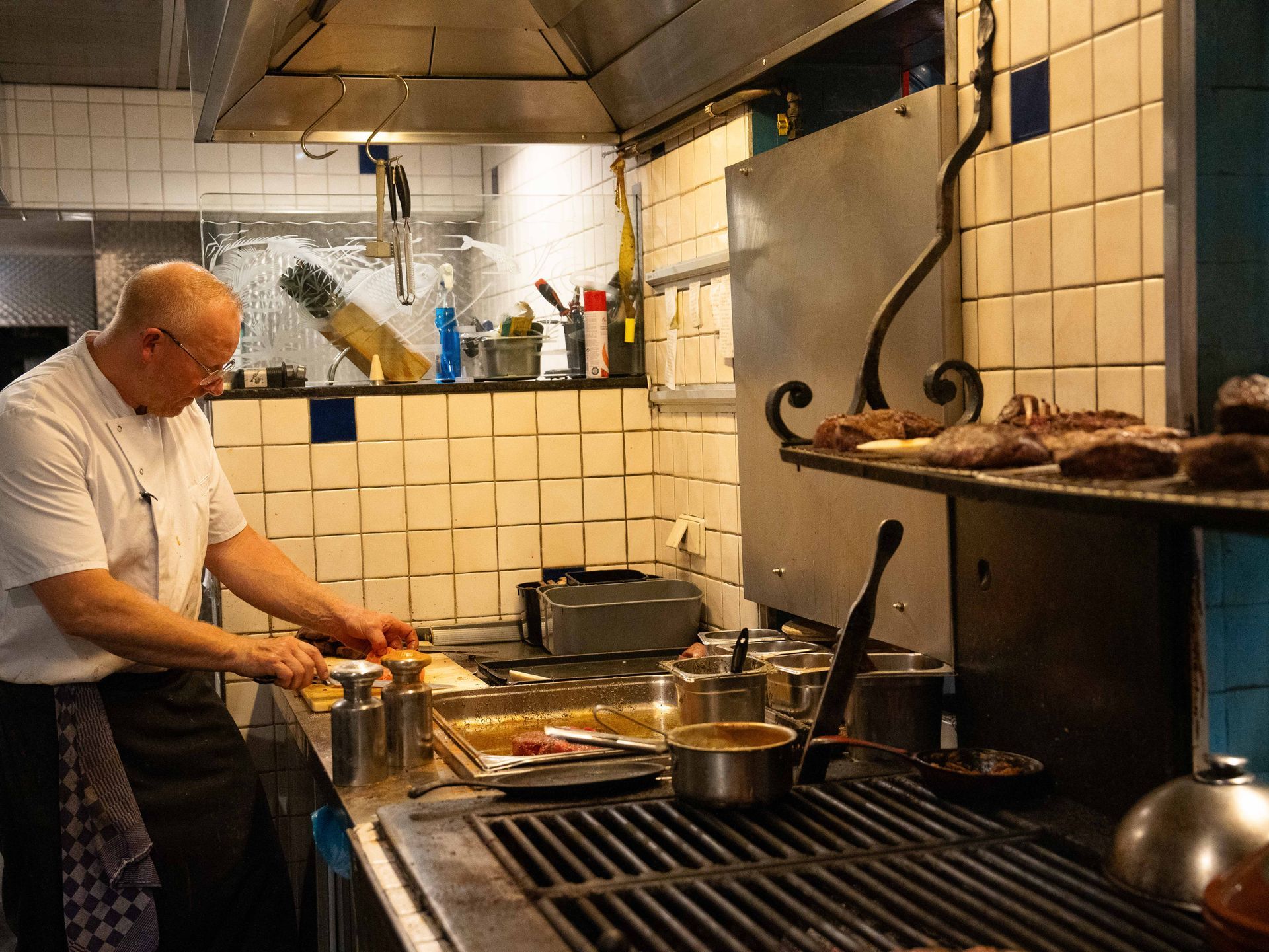 Een man staat in een keuken en bereidt eten op een grill.. Bij Linke Loetje