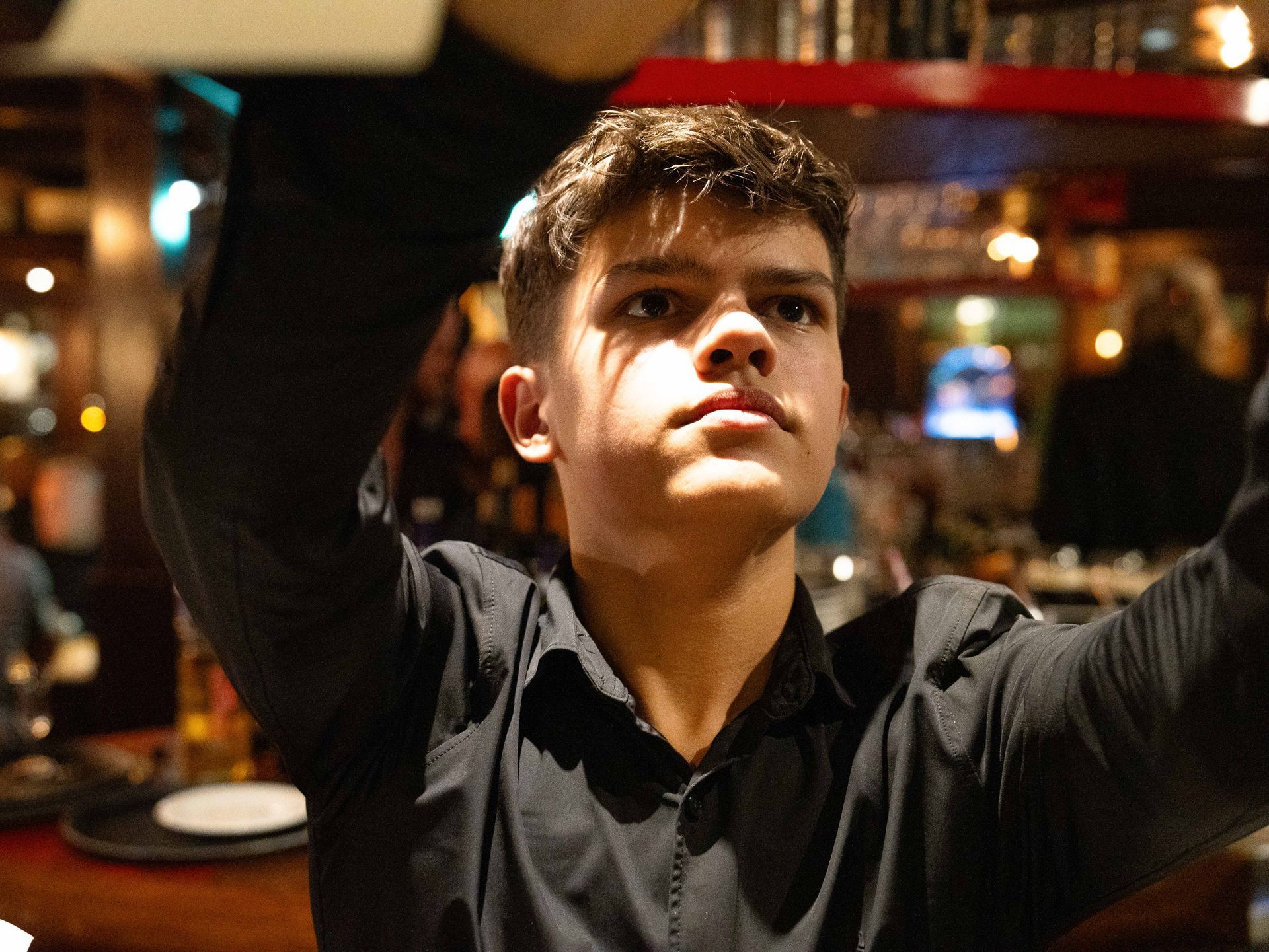 Een jongeman in een zwart overhemd kijkt naar iets op . Bij Linke Loetje