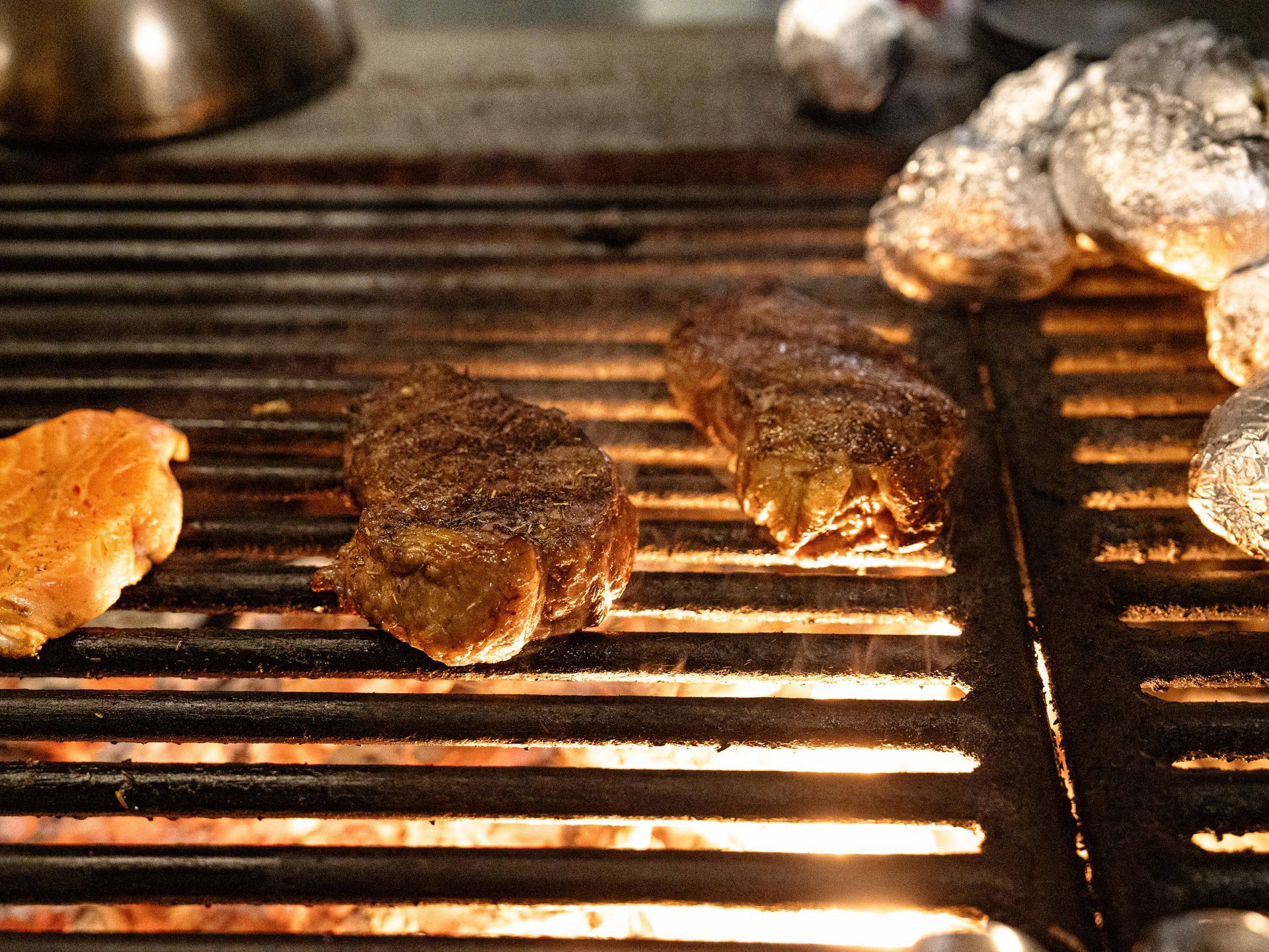 Twee steaks worden op een grill gebakken naast wat champignons . Bij Linke Loetje